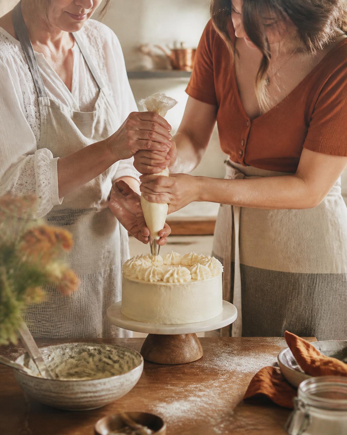A mother and daughter piping buttercream onto a cake together in their home kitchen